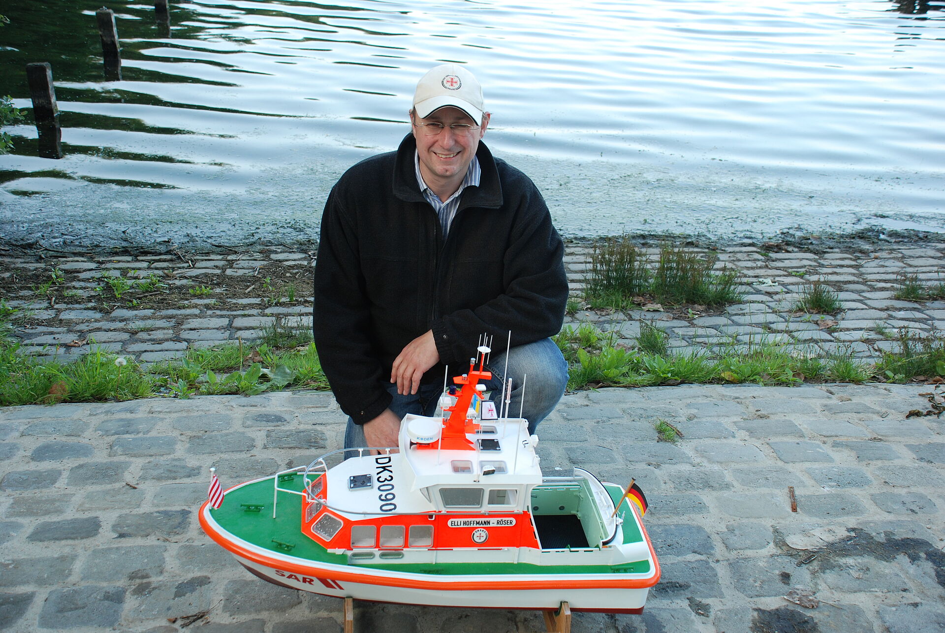 Ein Mann kniet hinter einem Modell eines Seenotrettungsbootes der DGzRS.